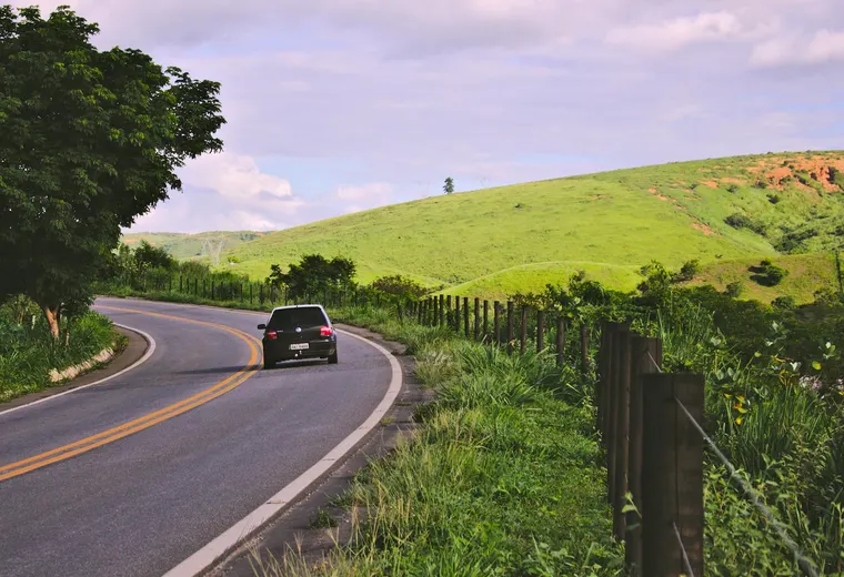 Car on a rural road in Brazil, surrounded by vegetation and hills.